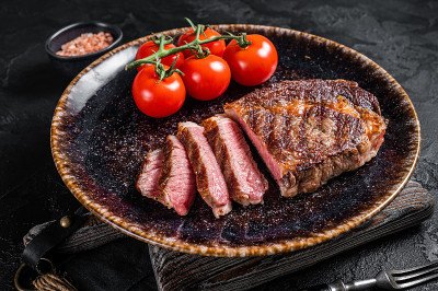 烤肋眼牛排，肋眼牛肉配番茄。黑色背景。俯视图