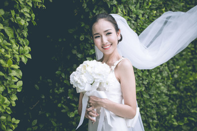 美丽迷人的亚洲新娘穿着婚纱微笑，手捧花束，在婚礼上感到骄傲和幸福