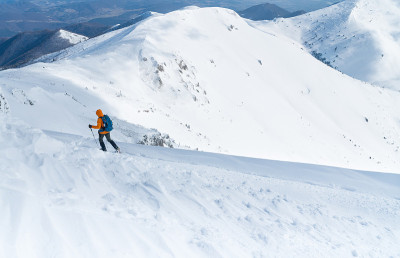登山运动员穿着亮橙色的软壳夹克，用登山杖从雪山山顶上下来。积极的人概念形象Velky Krivan，