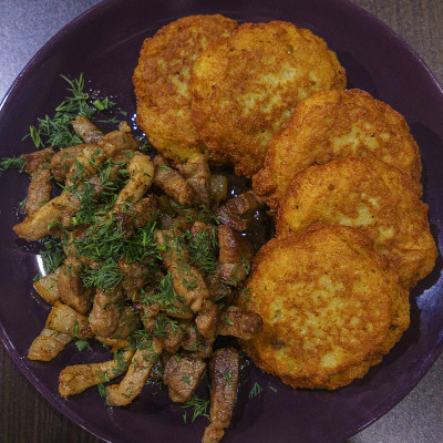 土豆煎饼和油炸肉在盘子上，在一个深色的木制背景。传统的斯拉夫美食。农村的概念。前视图。