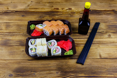 塑料盒子里的寿司卷，酱油和筷子放在木桌上。装在塑料容器内的寿司供外卖或运送