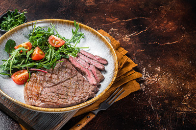 晚餐有烤牛肉、小牛肉、牛排和蔬菜沙拉。黑暗的背景。前视图。本空间