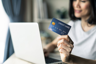 年轻美丽的亚洲女人拿着信用卡在家网上购物。2019冠状病毒病大流行期间，在家中使用笔记本电脑上网购物