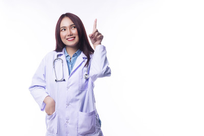 微笑的年轻女子医生制服大衣与听诊器，而使用手指指向一些孤立的白色背景。健康医疗理念。