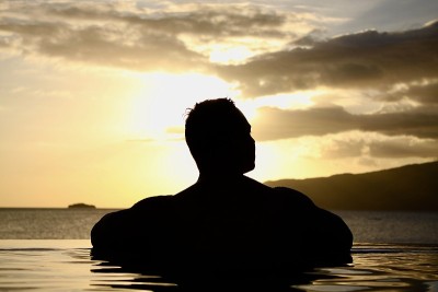 一个男人的剪影在一个无边的游泳池欣赏日落。