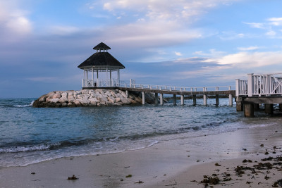 海滨Gazeebo日落海滩与海浪拍打海岸岩石。