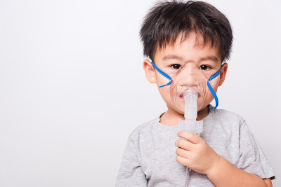 特写亚洲脸，生病的小孩他用蒸汽吸入器雾化面罩吸入自己的白色背景