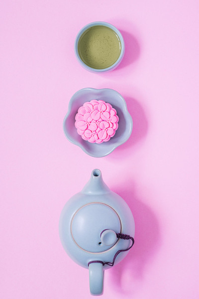 粉红色的月饼，蓝色的茶壶，粉红色背景上的一杯绿茶。中国的中秋节食品。