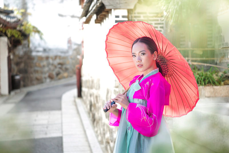 一个穿韩服戴粉红伞的韩国女孩。首尔著名的宫殿。美丽的女性穿着传统韩服在春天，老城首尔，韩国。