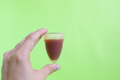 绿色背景上的女人手拿经血杯。空间的文本