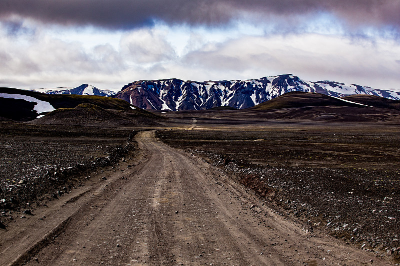 碎石路通往Landmannalaugar在冰岛与蓝色的雪山在阴天下的背景