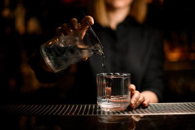 调酒师手拿水晶调酒杯，将鸡尾酒轻轻倒入老式透明玻璃杯中