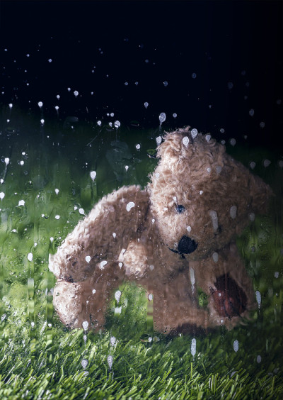 雨落在窗玻璃上。背景是孤独的棕色毛绒泰迪熊