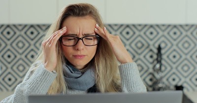 脸不高兴的年轻女子戴着眼镜坐在办公室的homa办公桌上揉太阳穴，闭着眼睛遭受头痛痛的感觉慢性偏头痛的