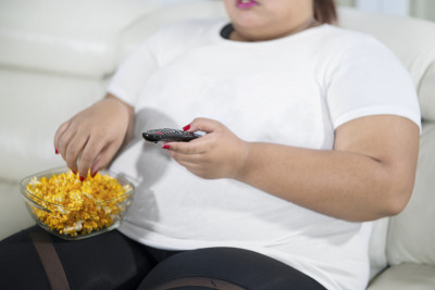 特写超重的亚洲妇女与一碗爆米花看电视