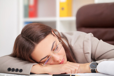 年轻疲惫的女人在办公室闭眼睡觉，睡眠剥夺和充满压力的生活观念