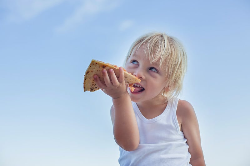 Sweet toddler child, eating pizza on the beach, ha