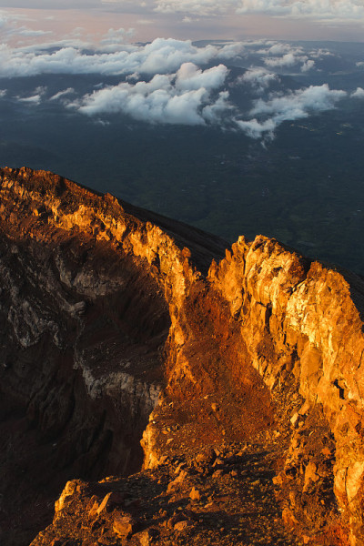 在巴厘岛日出峰顶的阿贡火山边缘。云朵之上，五彩缤纷的风景。初升太阳的第一缕阳光是橙色的。阿贡火山顶部
