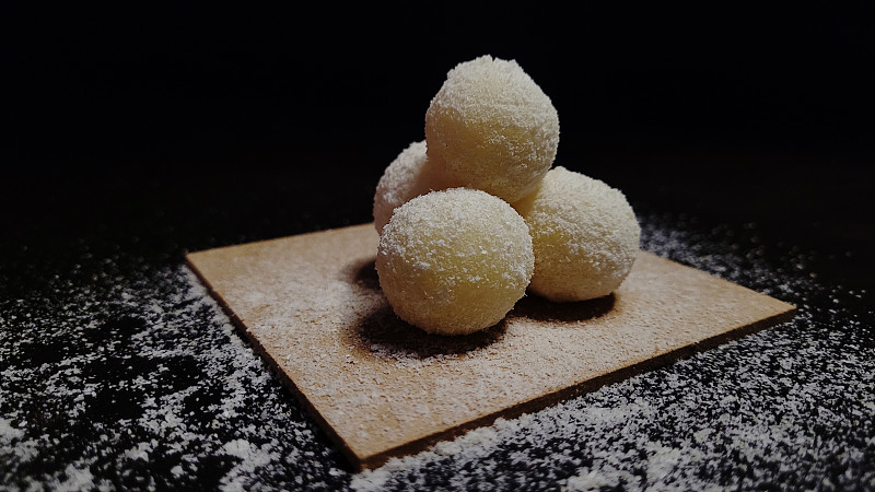黑色背景木板上的雪球圣诞糖果，椰子屑，牛奶糖果的特写，米浆韩国甜点，健康甜点，椰子汁糖果，素食甜点