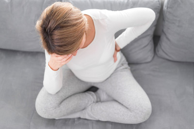 怀孕疲惫不堪的女人带着肚子和头的问题躺在家里的沙发上，生病了。