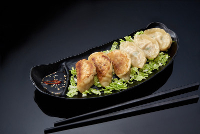 亚洲美食:黑色盘子里的煎饺，黑色背景上涂着酱油