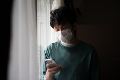 一位生病的日本男子戴着医用口罩站在窗边