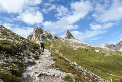 一名女子背着背包，拄着拐杖在意大利Dolomites的一条狭窄小路上徒步旅行。那里有陡峭的山。在一个