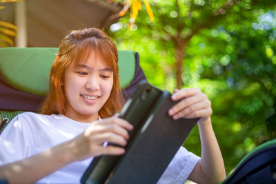 快乐的亚洲妇女坐在折叠椅上使用平板电脑在公园。