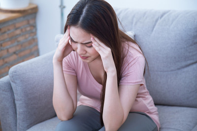 年轻女子在家里的沙发上痛苦地用手捂着头。年轻女性患有严重的偏头痛。