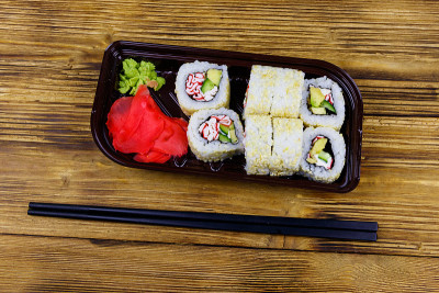 浦崎寿司卷和鱼糜装在塑料盒里放在木桌上。前视图。装在塑料容器内的寿司供外卖或运送