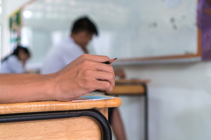 教育考试考试的概念，高中/大学学生拿着铅笔写纸答题纸坐在椅子上，在考场或教室参加考试。教育评价理念