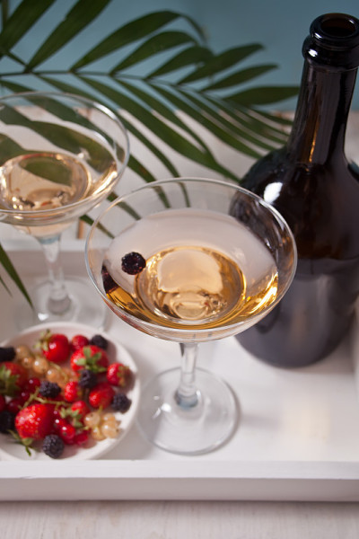 白葡萄酒装在玻璃杯、瓶子和盘子里，白色的木托盘上放着浆果。晚餐有两个。