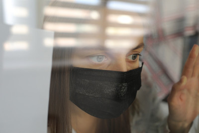 年轻女子戴着医用口罩，躲在家里的窗户后面。冠状病毒大流行、冠状病毒19的检疫概念。有选择性的重点