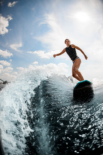看女人谁骑在wake surf在高浪对蓝色的天空