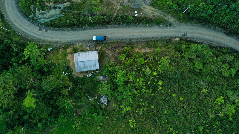 在森林里的一条土路旁边，一个铁皮屋顶的房子的顶视图