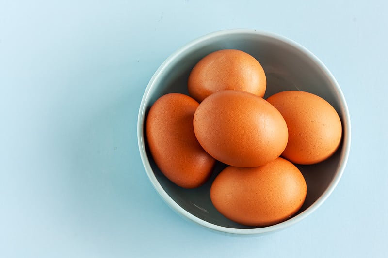 Fresh organic raw eggs in blue bowl on light paste