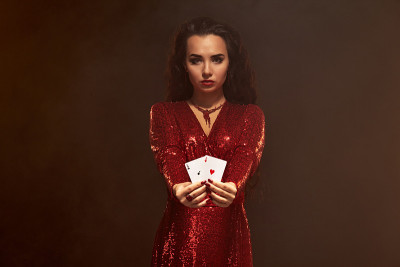 年轻美丽的幸运黑发女郎穿着红色晚礼服展示她的卡片，一对王牌