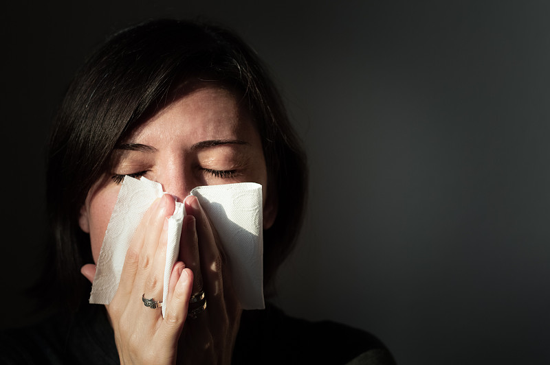 一个患感冒的女人用手帕擤鼻子的肖像