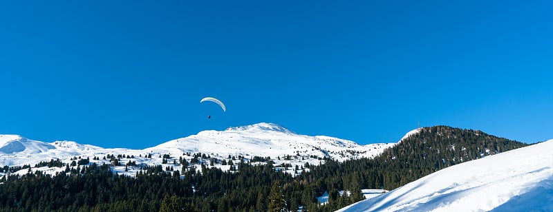 全景冬季山地景观与雪山山峰和滑翔伞在蓝天之上