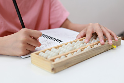 裁剪图像的亚洲学生使用算盘做计算。