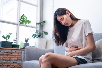 亚洲年轻女子食物中毒。她坐在家里的沙发上。女性有胃痛和痉挛。女孩感到如此痛苦，悲伤和孤独。保健食品和