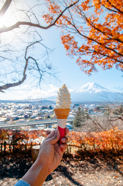 手拿软冰淇淋蛋筒与富士山和色彩斑斓的秋天枫树背景