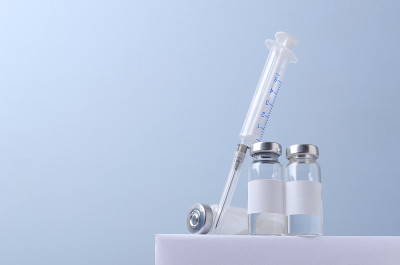 蓝色背景下的白色支架上放着三瓶疫苗和注射器。空的空间