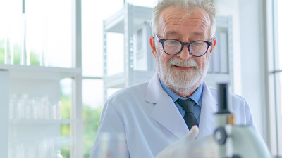 高级男性研究员在实验室里专注地思考科学研究。具有前景的仪器测试烧杯和试管放在桌上