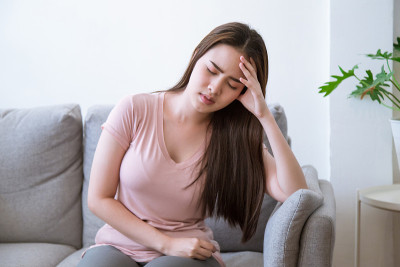 年轻女子手捧额头，头痛地坐在沙发上。年轻女性患有严重的偏头痛。