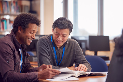 教师与成年男性学生坐在桌子旁在大学图书馆工作
