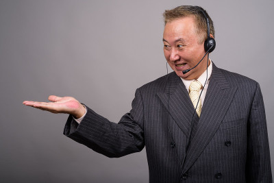 灰色背景下，在呼叫中心工作的成熟亚洲商人的摄影