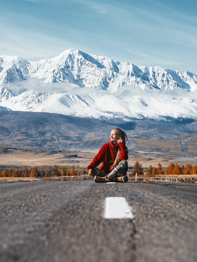 坐在山路上的旅行女子。美丽的雪峰背景。旅游的概念
