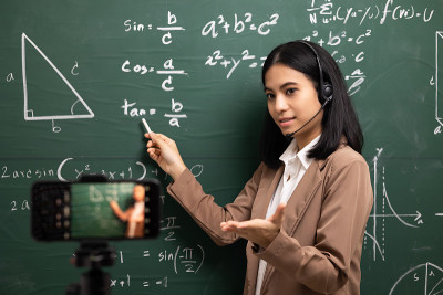 年轻的亚洲女教师站在摄像机和学生视频会议。女教师在课堂上通过智能手机在线课程直播培训数学。