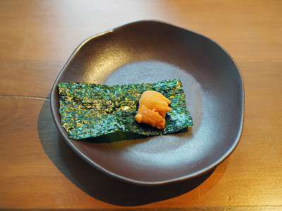 新鲜的海胆生鱼片与一层干海带放在黑色的盘子里一起食用。